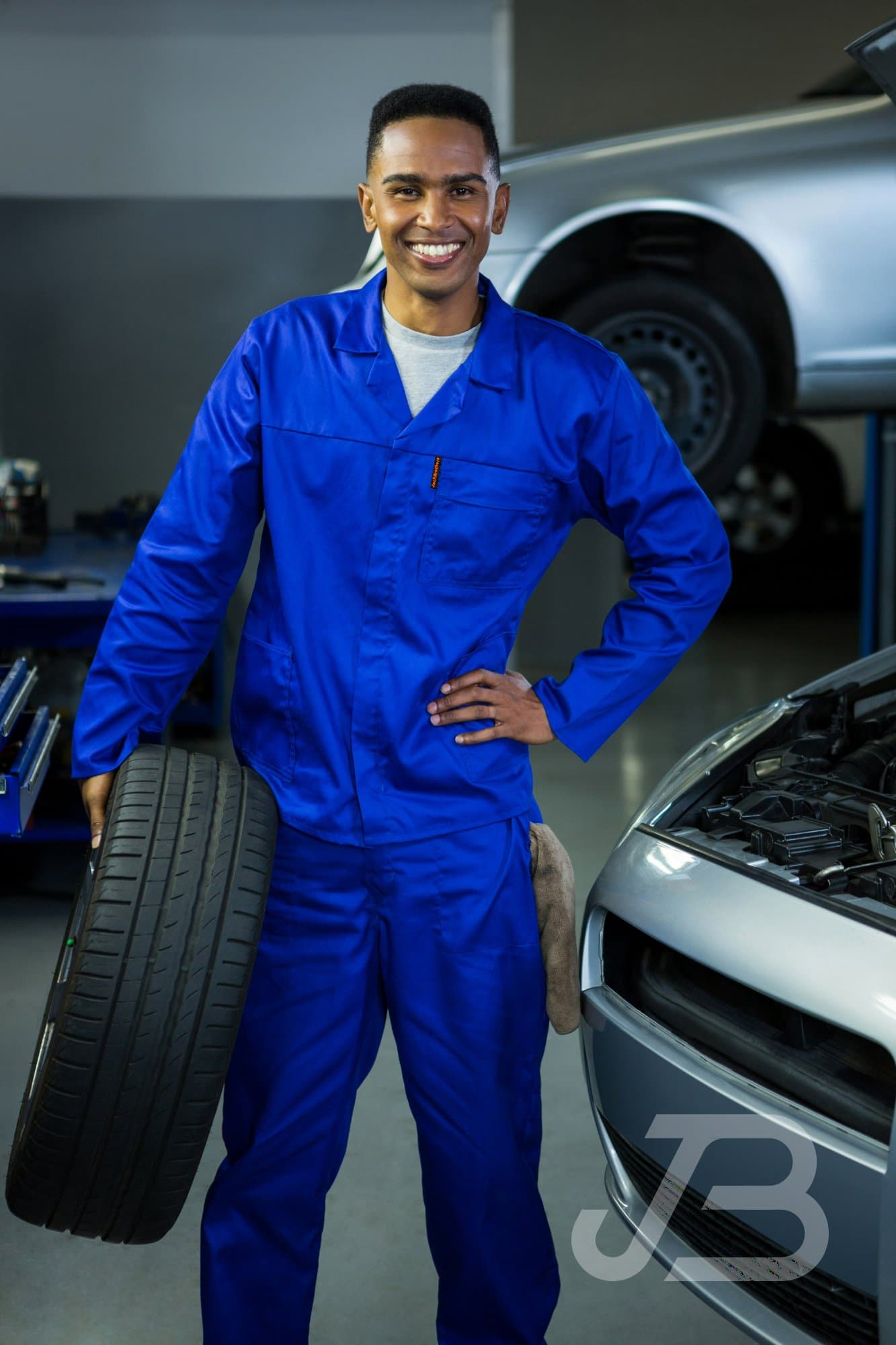 Mechanic in a royal blue overall holding a tyre in a workshop