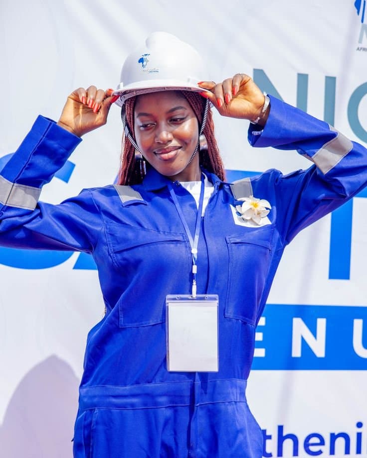 Woman in a royal blue overall with reflective tape adjusting a white hard hat